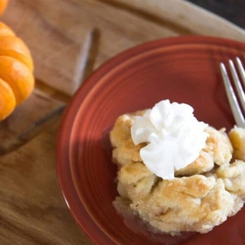 Old fashioned apple dumpling topped with whipped cream on a red plate